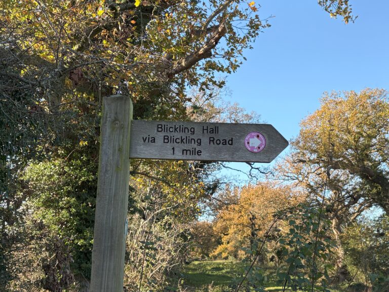 A wooden signpost on a sunny day points to Blickling Hall via Blickling Road, 1 mile away. This is one of two easy day trips from Norwich England