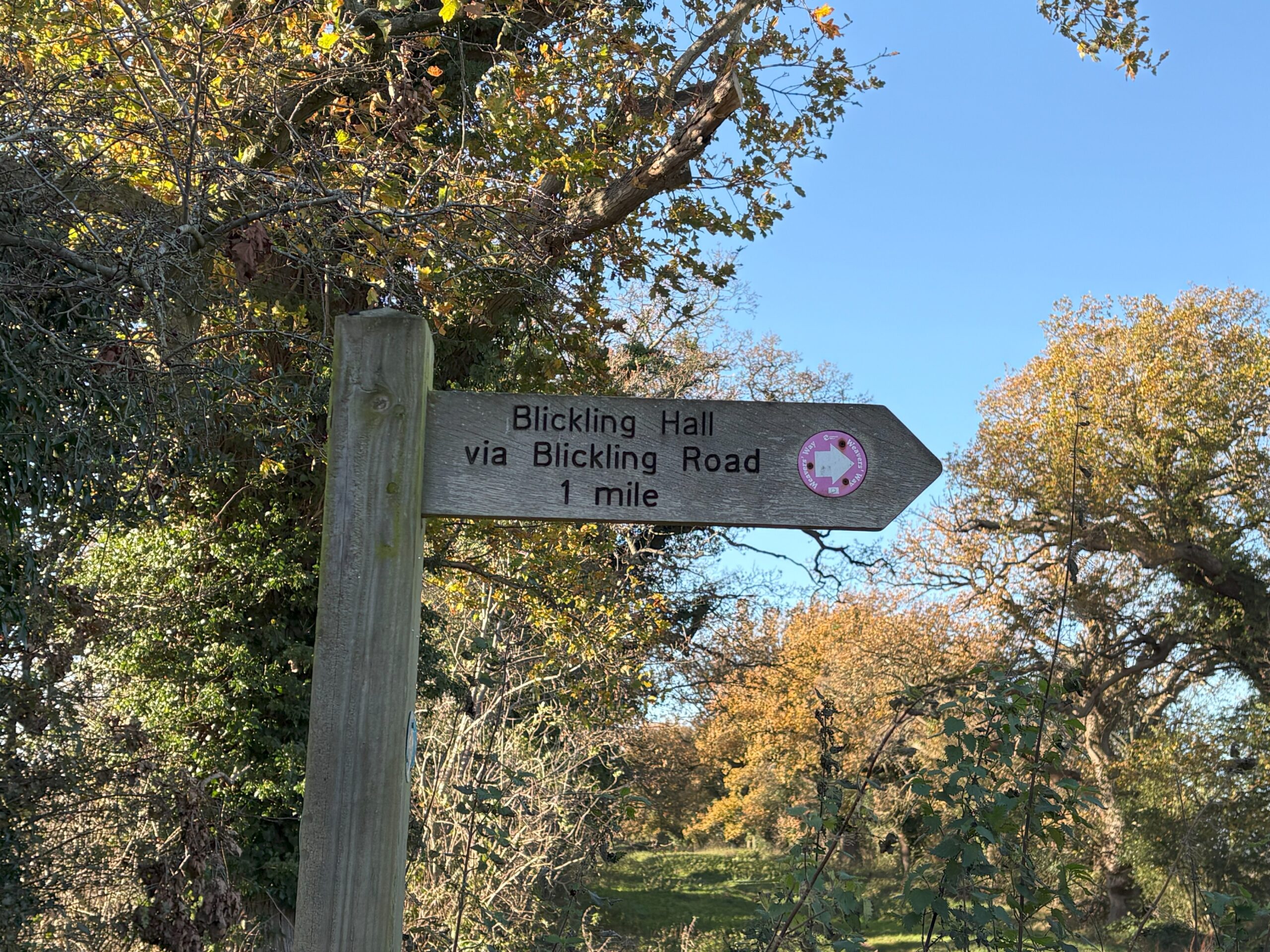 A wooden signpost on a sunny day points to Blickling Hall via Blickling Road, 1 mile away. This is one of two easy day trips from Norwich England