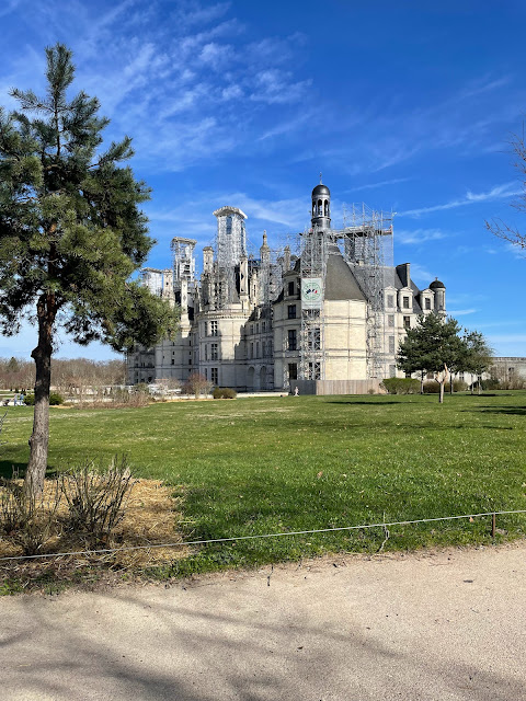 A large, historic building under renovation is shrouded in scaffolding, a reminder of travel mistakes when planning an off-season visit. It stands proudly amid green grass and trees under a clear blue sky, with a lone tree gracing the left foreground.