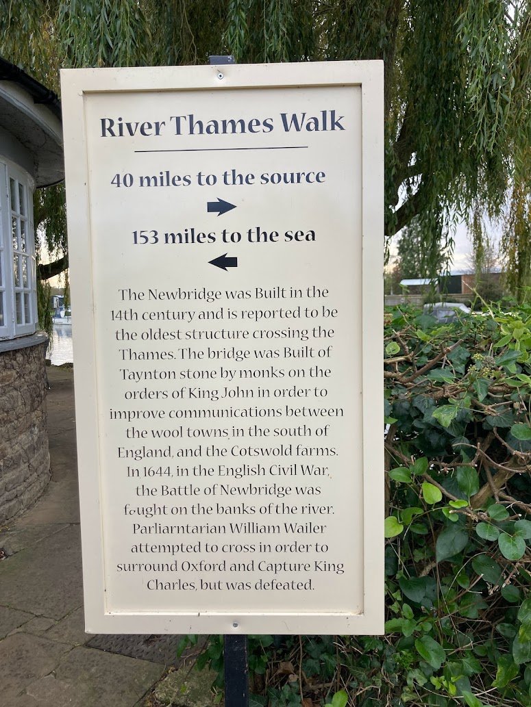A sign titled River Thames Walk gives distances to the river’s source (40 miles) and the sea (153 miles), and provides historical information about Newbridge, the English Civil War, and King Charles.
