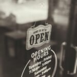 A classic 'Come in, we're open' sign on a glass door in a Bali café with opening hours displayed.