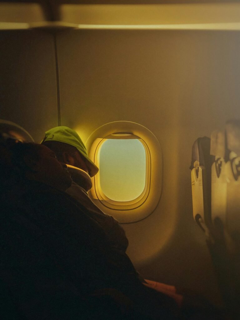 A person rests peacefully by an airplane window, warm light filtering through.